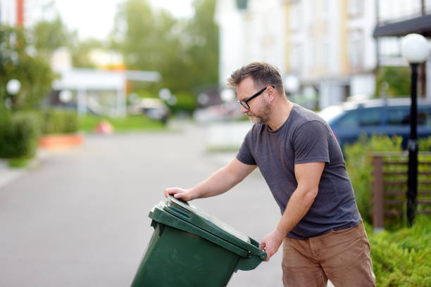 A person opening a green bin outside a home, ready to move it to the curb.
