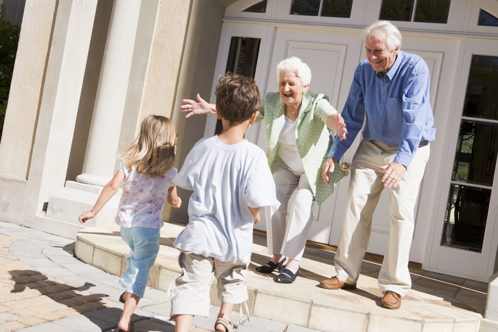 Grandparents happily welcoming their grandchildren at the front door of their home.