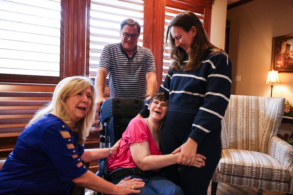 Caregivers sharing a warm moment with a young person using a wheelchair in a comfortable living room.
