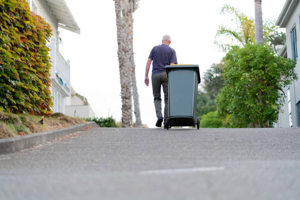 A resident walking a wheeled bin up a long driveway toward the street.