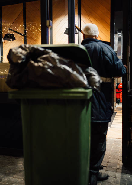 An overfilled household bin with a full bag balanced on top at dusk.